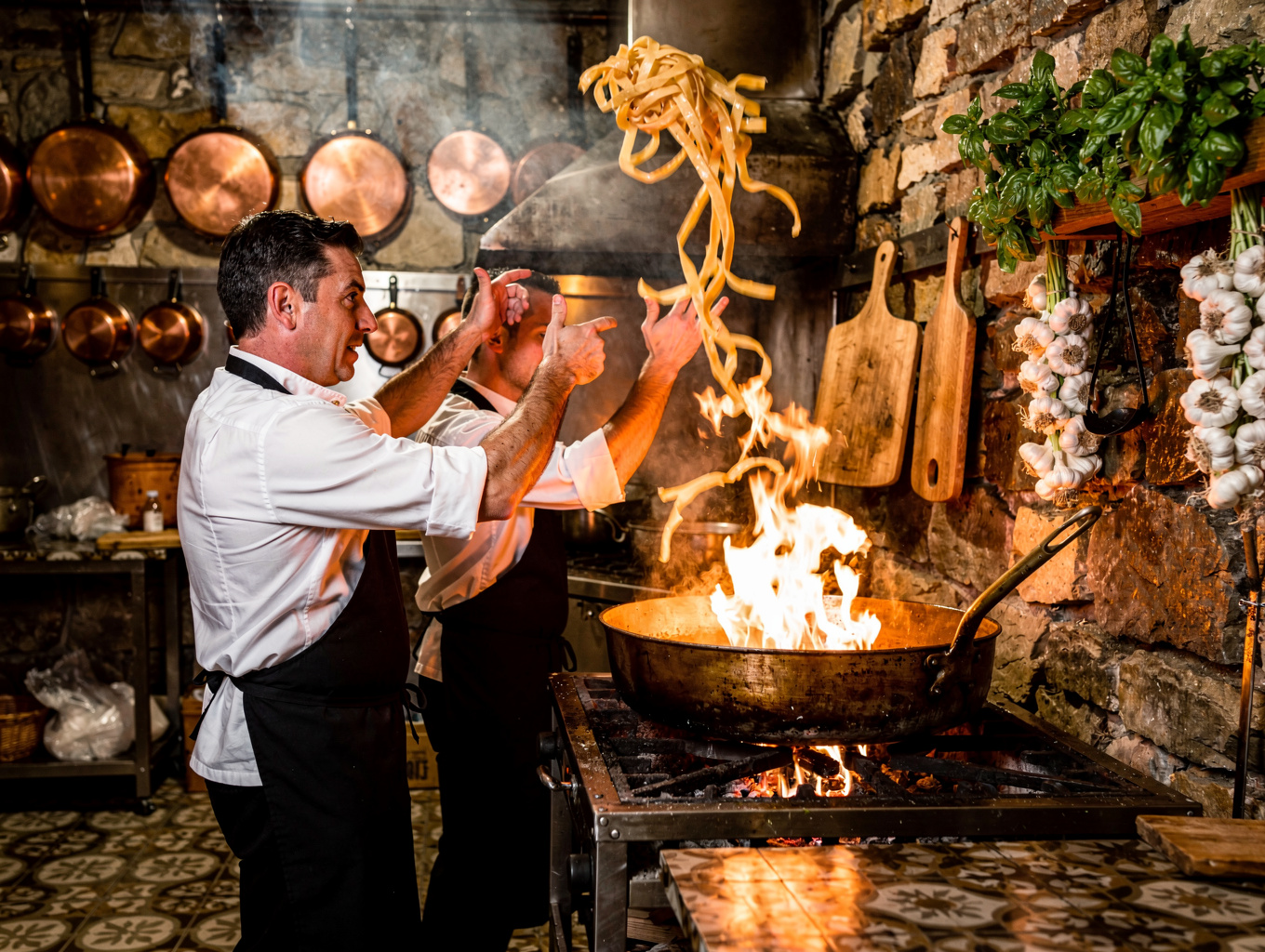 Chefs preparing fresh handmade pasta over glowing wood embers in the open kitchen